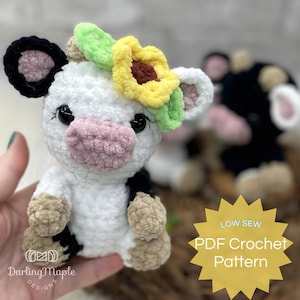 May include: A crocheted plush cow toy with black and white spots, a pink nose, and a yellow sunflower with green leaves on its head. The toy is sitting on a wooden surface. LOW SEW PDF Crochet Pattern.