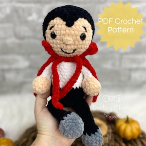 May include: PDF crochet pattern for a cute amigurumi vampire doll with black hair, a red cape, and a white shirt. The doll is sitting with its legs crossed and has a friendly smile.
