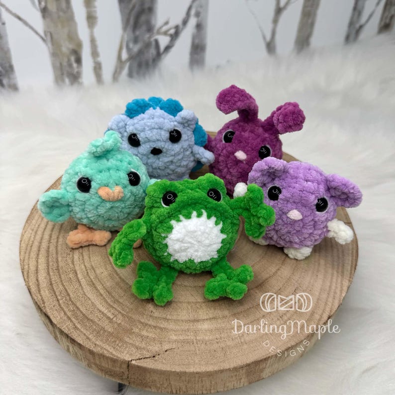 K&ouml;nnte beinhalten: F&uuml;nf kleine, runde, flauschige H&auml;keltiere in verschiedenen Farben: ein hellblauer Igel, ein violetter Hase, ein mintgr&uuml;ner Vogel, ein hellgr&uuml;ner Frosch mit wei&szlig;em Bauch und ein hellviolettes Wesen mit gro&szlig;en Ohren, alle mit schwarzen Sicherheitsaugen.