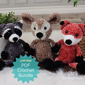 Peut inclure: Trois jouets en peluche crochetés en forme d'animaux : un raton laveur, un cerf et un renard. Le raton laveur est gris et noir, le cerf est marron et le renard est rouge et blanc. Les jouets font partie d'un lot de crochet.