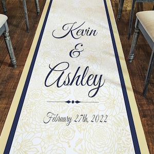 May include: A white aisle runner with a navy blue border and gold accents. The runner features a floral pattern and the text "Kevin & Ashley" with the date "February 27th, 2022".