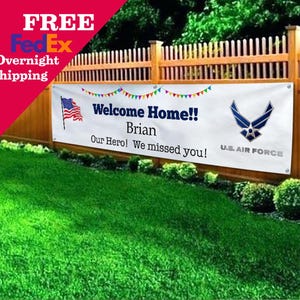 Peut inclure: Une banni&egrave;re blanche avec le texte "Welcome Home!! Brian Our Hero! We missed you !" et un embl&egrave;me de l'US Air Force. Un drapeau am&eacute;ricain est &agrave; gauche. La banni&egrave;re est accroch&eacute;e &agrave; une cl&ocirc;ture en bois.