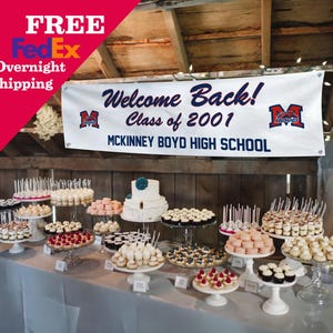 May include: A dessert table with a variety of treats, including a tiered white cake with a blue flower, cupcakes, macarons, and other pastries. A banner reads "Welcome Back! Class of 2001 McKinney Boyd High School."