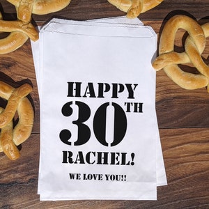 Może przedstawiać: Biała papierowa torba prezentowa z czarnym tekstem, kt&oacute;ry brzmi "Happy 30th Rachel! We love you!!"