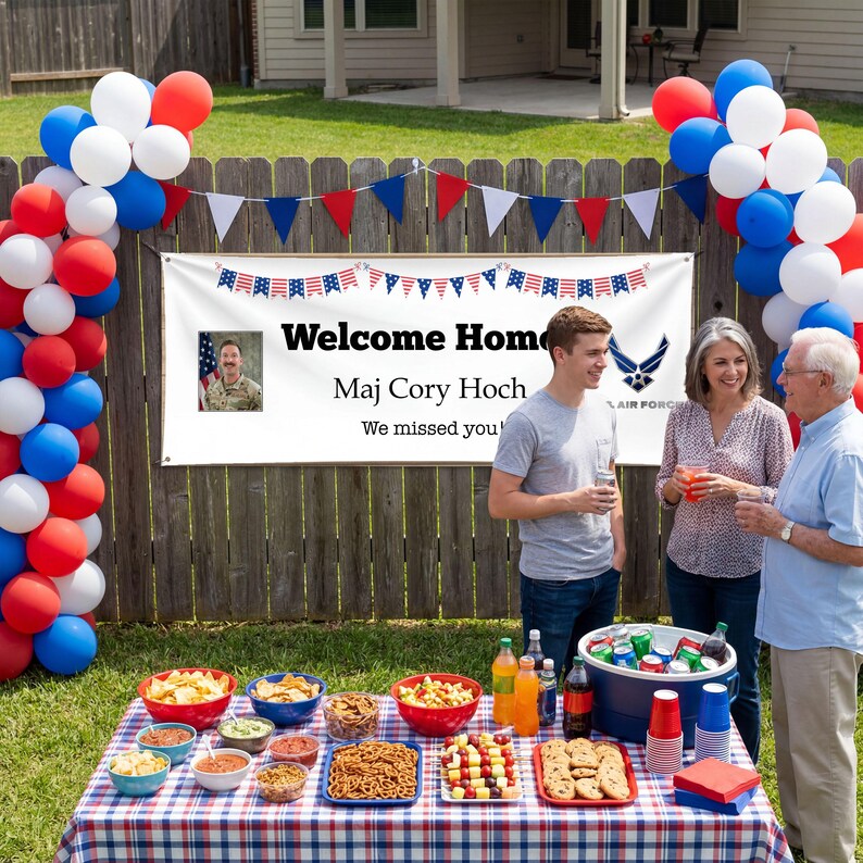 Peut inclure: Sc&egrave;ne de f&ecirc;te dans un jardin avec une banni&egrave;re "Welcome Home Maj Cory Hoch". Des ballons et des d&eacute;corations rouges, blancs et bleus sont pr&eacute;sents. Une table est dress&eacute;e avec des collations et des boissons, et des gens sont rassembl&eacute;s.
