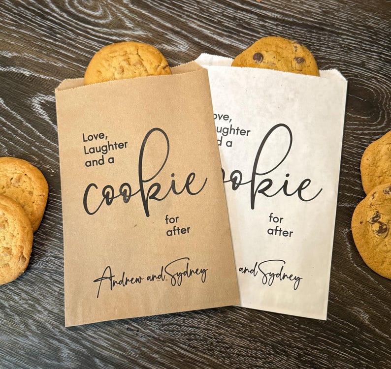 Op de afbeelding: Twee papieren koekjeszakjes, &eacute;&eacute;n bruin en &eacute;&eacute;n wit, elk met een koekje erin. De zakjes hebben de tekst "Love, Laughter and a Cookie for after" en de namen "Andrew and Sydney" erop gedrukt. Er liggen meerdere koekjes.