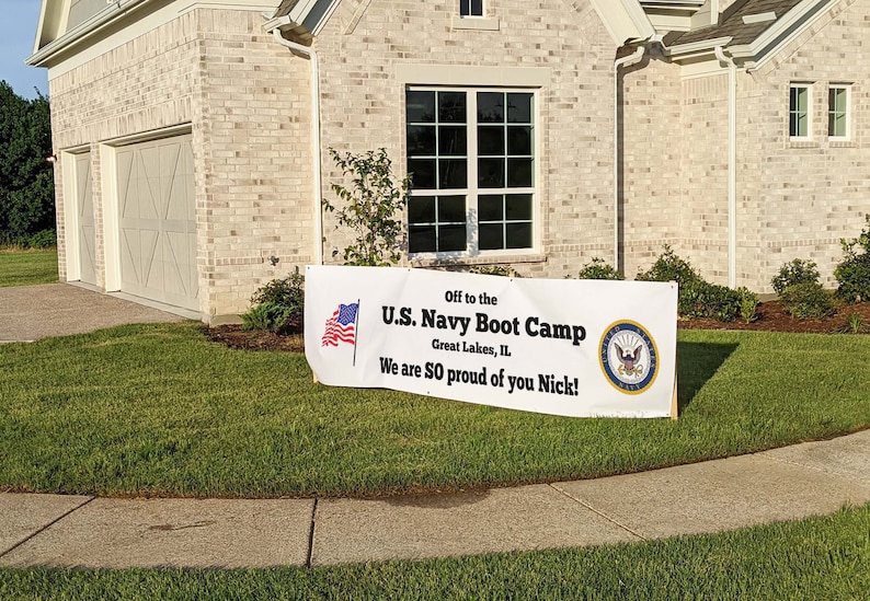 Peut inclure: Une banni&egrave;re blanche sur une pelouse indique : "Off to the U.S. Navy Boot Camp, Great Lakes, IL. We are SO proud of you Nick !" Un drapeau am&eacute;ricain et l'embl&egrave;me de la marine sont &eacute;galement affich&eacute;s. La banni&egrave;re est devant une maison.