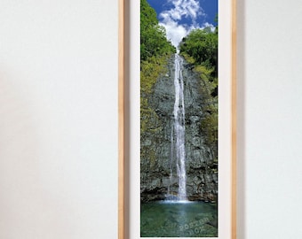 May include: A vertical framed wall art print featuring a tall, narrow waterfall cascading down a dark, textured rock cliff face surrounded by lush green trees under a bright blue sky with white clouds. The text POSTER BOX is visible at the bottom.