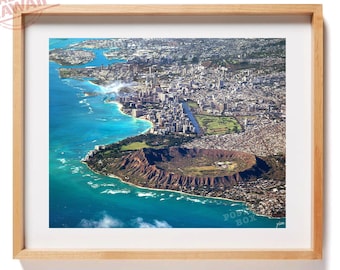 May include: An aerial photograph of the Honolulu coastline and Diamond Head crater, framed in light wood. The image displays the blue ocean, urban buildings, and the volcanic landscape. A stamp in the corner reads MADE IN HAWAII.