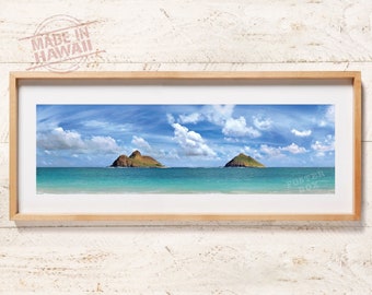 May include: A panoramic photograph of two small islands in the ocean with a blue sky and white clouds. The water is a turquoise color and the islands are green. The image is framed in a light wood frame.