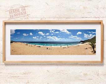 May include: A panoramic photograph of a sandy beach with turquoise ocean waves, a blue sky with white clouds, and people scattered across the shore, enclosed in a light-colored wooden frame with the text MADE IN HAWAII visible in the corner.