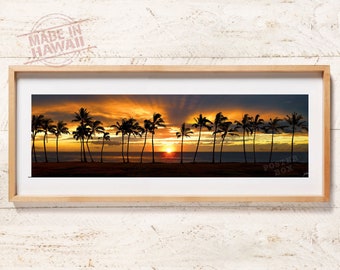 May include: A panoramic framed print featuring a sunset over the ocean with silhouettes of palm trees along the horizon. The sky displays vibrant orange and yellow hues. The text MADE IN HAWAII and POSTER BOX are visible on the print.