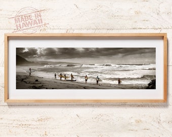 May include: A panoramic black and white photograph in a light wood frame depicting a sandy beach with several individuals holding surfboards, looking out toward large ocean waves under a cloudy sky. The text MADE IN HAWAII is visible.