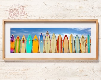 May include: A panoramic framed wall art print featuring a row of fourteen colorful surfboards standing upright against a bright blue sky with light clouds. The surfboards display various patterns, including solid colors, stripes, and graphic designs.