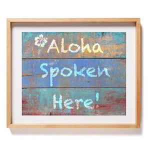 May include: A framed wall art print featuring a weathered, multi-colored wooden plank background with the text "Aloha Spoken Here!" painted in white and light blue, accompanied by a white hibiscus flower icon on the top left corner.