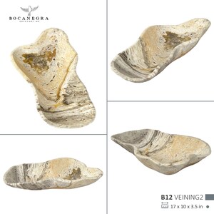 May include: A natural stone decorative bowl with a unique, organic shape. The bowl features a blend of beige, cream, and gray tones with a marbled effect. The dimensions are 17 x 10 x 3.5 inches.
