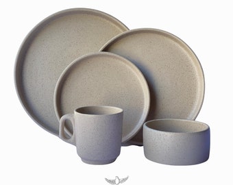 May include: A set of speckled beige ceramic dinnerware, including a large plate, a medium plate, a bowl, and a mug. The set is arranged on a white background. The brand name "BOCANEGRA ONYX ART MX" is printed below the set.