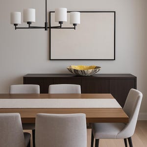 May include: A modern dining room scene featuring a wooden table with a light-colored runner, surrounded by gray upholstered chairs. A dark wood cabinet holds a decorative bowl. Above, a black framed artwork and a black chandelier with white shades.