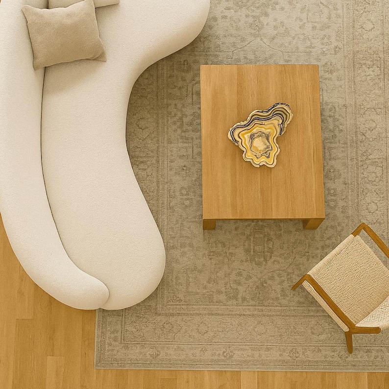 May include: An overhead view of a modern living room with a cream-colored sofa, a wooden coffee table, and a patterned rug. A decorative stone piece sits on the table. A chair with a woven seat is in the corner.