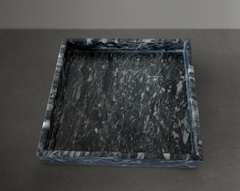 May include: A square black marble tray with a white veined pattern. The tray has a raised edge.