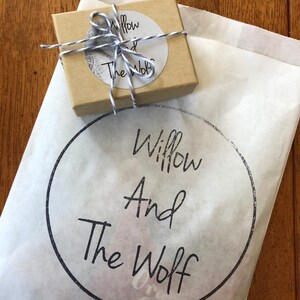Puede incluir: Una bolsa de papel marr&oacute;n con un logotipo circular blanco que dice "Willow And The Wolf". La bolsa est&aacute; atada con una cuerda blanca y tiene una peque&ntilde;a caja marr&oacute;n dentro.
