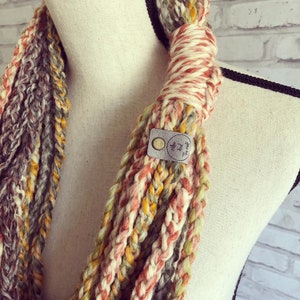 Puede incluir: Una bufanda infinita de crochet multicolor con una etiqueta de cuero marr&oacute;n que dice "Wild and The Wife".