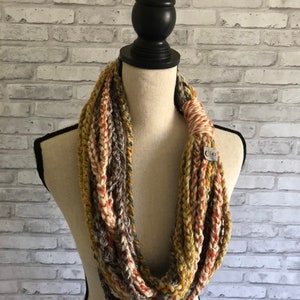 Puede incluir: Una bufanda infinita de ganchillo en tonos marrones, beige y naranja. La bufanda est&aacute; hecha con un hilo grueso y tiene un punto simple y texturizado.
