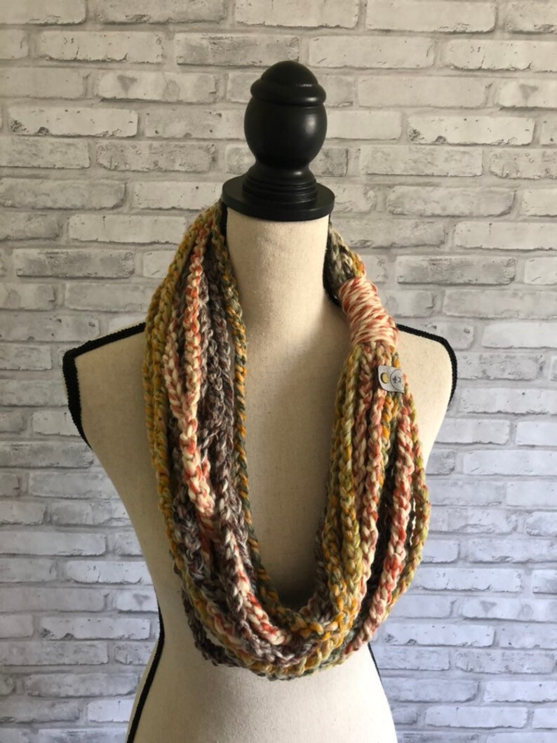 Puede incluir: Una bufanda infinita de ganchillo en tonos marrones, beige y naranja. La bufanda est&aacute; hecha con un hilo grueso y tiene un punto simple y texturizado.