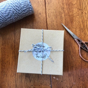 Puede incluir: Una caja de regalo marr&oacute;n envuelta con hilo blanco y azul y una etiqueta redonda que dice "Willow and The Wolff".