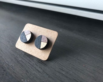 Puede incluir: Un par de pequeños pendientes redondos de madera con un diseño geométrico. Los pendientes son negros, blancos y dorados.