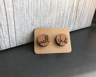 Puede incluir: Un par de pendientes de madera con las palabras "well" y "shut" grabadas en ellos. Los pendientes están en una tarjeta marrón.