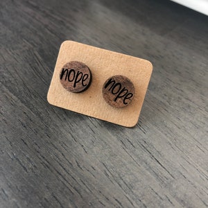 Puede incluir: Un par de pendientes de madera con la palabra "nope" grabada en cada pendiente.