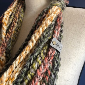 Puede incluir: Una bufanda infinita de crochet multicolor con una etiqueta de cuero marr&oacute;n que dice "Made with Love" en letras blancas.