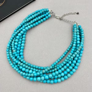 May include: A turquoise blue multi-strand necklace made of round beads. The necklace has a silver clasp.