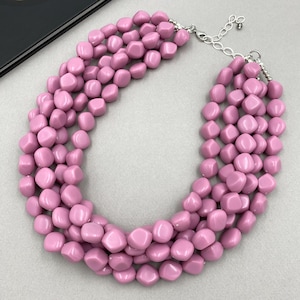 May include: A chunky, multi-strand necklace featuring large, rounded, light pink beads. The necklace has a silver-toned chain and clasp for adjustable length. The beads are evenly spaced and create a bold, statement piece of jewelry.