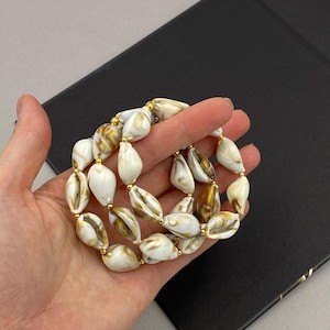 May include: A white and gold shell necklace with gold beads. The necklace is made of multiple strands of shells.