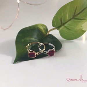 May include: Two wire rings with red square-shaped gemstones. The rings are on a green leaf. The rings are made of gold and silver wire.