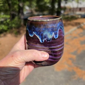 Puede incluir: Un vaso de cerámica hecho a mano con un esmalte único. Los colores transitan del morado intenso al azul vibrante, con toques dorados en el borde. La superficie texturizada se suma a su atractivo artesanal. Perfecto para disfrutar de tu bebida favorita.