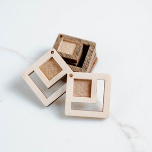 May include: Three wooden square shapes with cutouts. The top shape is stacked on top of two other shapes. The top shape is light brown, the middle shape is dark brown, and the bottom shape is light brown.