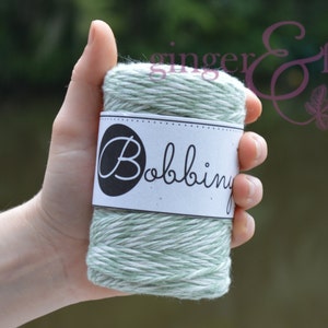 May include: A roll of green and white twine with a white label that says "Bobbiny".