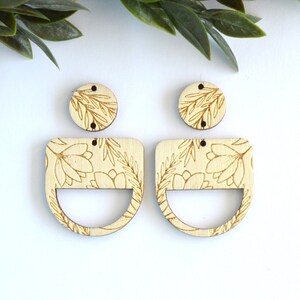 May include: A pair of wooden earrings with a floral design. The earrings are in the shape of a half-circle with a smaller circle in the center. The floral design is etched into the wood.