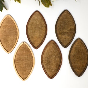 May include: Six wooden teardrop-shaped earrings in varying shades of brown. The earrings have a light-coloured wood grain centre with a darker wood border. Each earring has a small hole at the top for hanging. The earrings are displayed on a white surface.