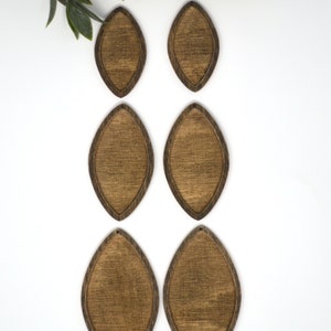 May include: Six wooden teardrop-shaped earring blanks with a dark brown stain and a lighter brown centre. The earrings are arranged on a white surface, with green leaves in the upper left corner.