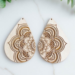 May include: A pair of wooden teardrop-shaped earrings with a laser-cut mandala design. The earrings are a light brown color and have a hole at the top for attaching earring hooks.