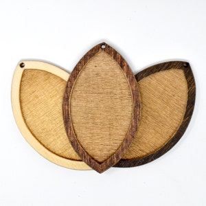 May include: Three wooden leaf-shaped blanks with a natural wood finish. The center blank is a darker brown color. The blanks have a hole at the top for hanging.
