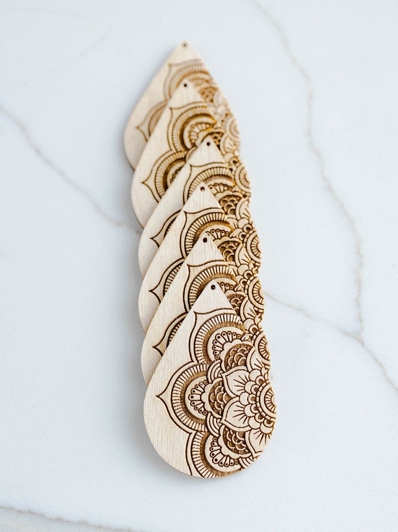 May include: Five unfinished wooden teardrop-shaped earrings with intricate laser-cut mandala designs.