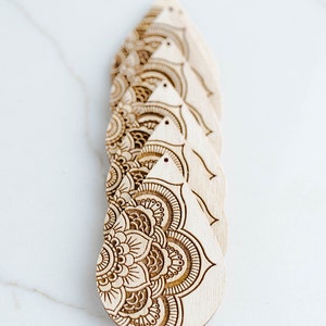 May include: Five wooden teardrop-shaped earrings with intricate laser-cut mandala designs. The earrings are stacked on top of each other, with the bottom earring showing the most detail.