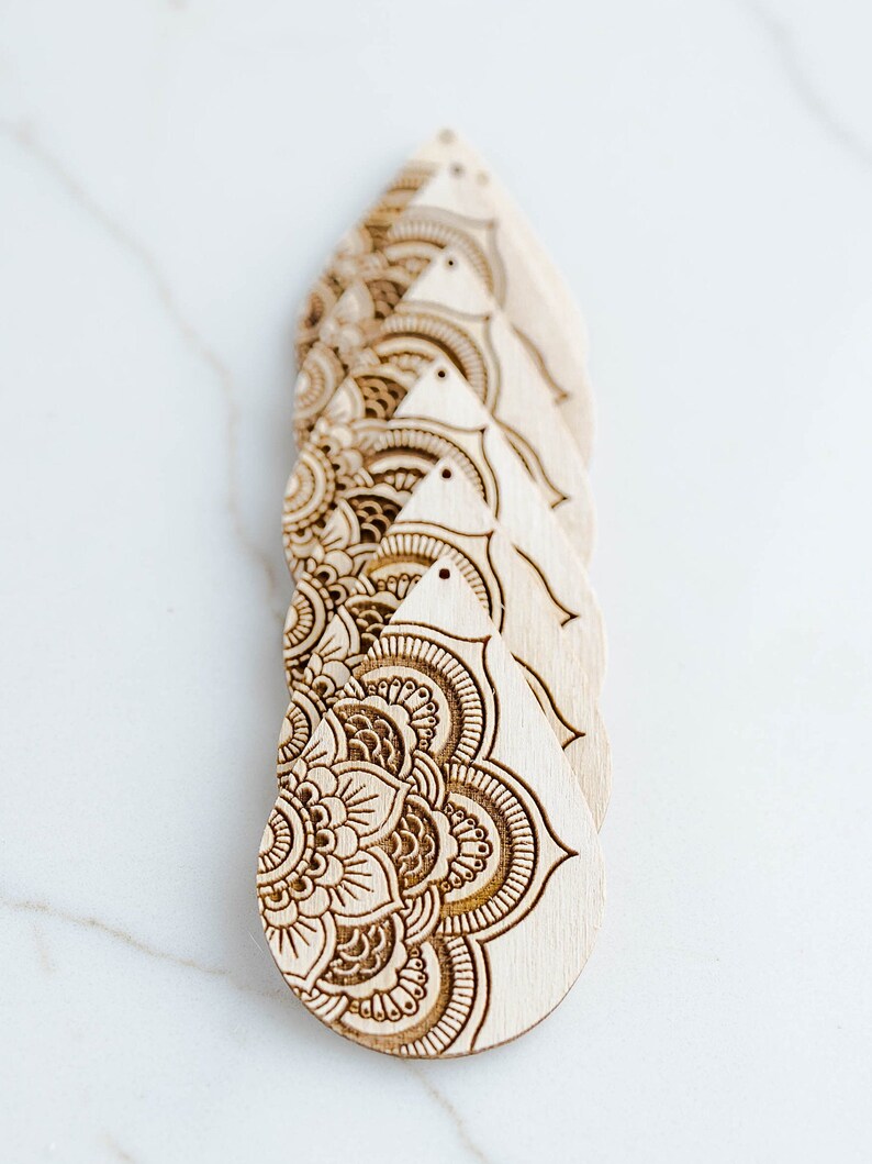May include: Five wooden teardrop-shaped earrings with intricate laser-cut mandala designs. The earrings are stacked on top of each other, with the bottom earring showing the most detail.