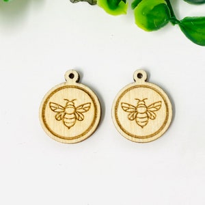 May include: Two wooden circle charms with a laser-cut design of a bee in the center. The charms are unfinished and ready to be painted or stained.