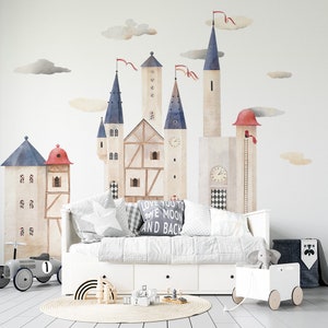 Pode incluir: Um sofá branco com uma manta e almofadas de padrão cinza e branco. A parede atrás do sofá tem um mural de aquarela caprichoso de um castelo com detalhes azuis e vermelhos. O mural inclui nuvens e o texto "Love you to the moon and back".